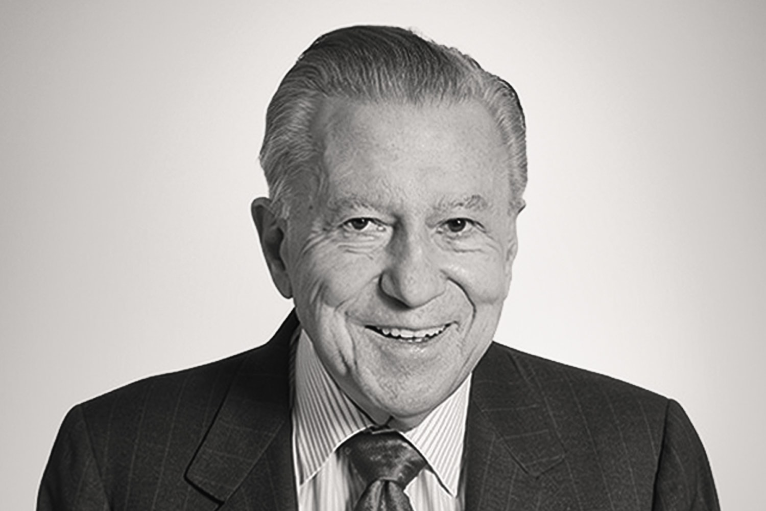 Portrait of Bill Pollock, founder of Drake International, smiling, in a pinstripe suit and tie