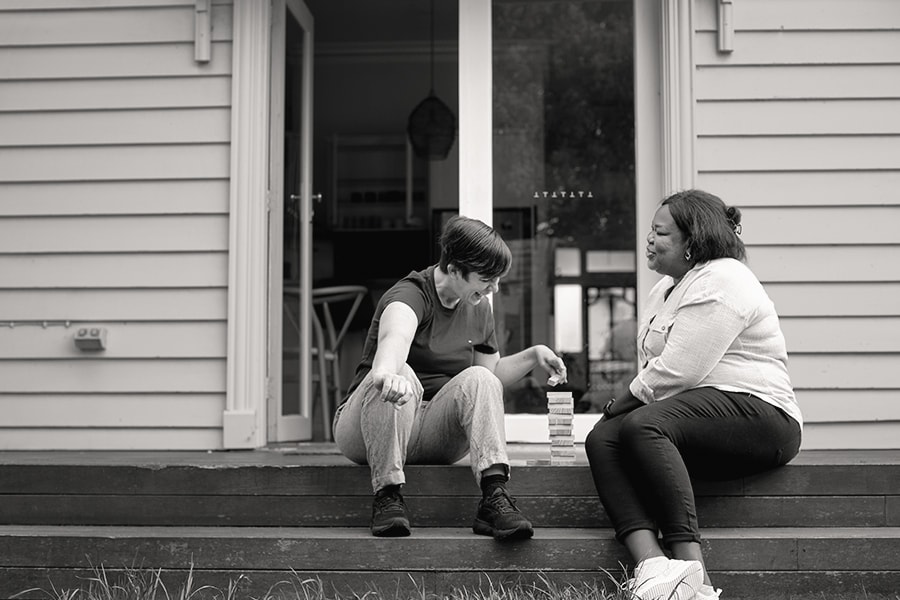 A support worker and a woman playing a stacking-block game together on the back steps of a house