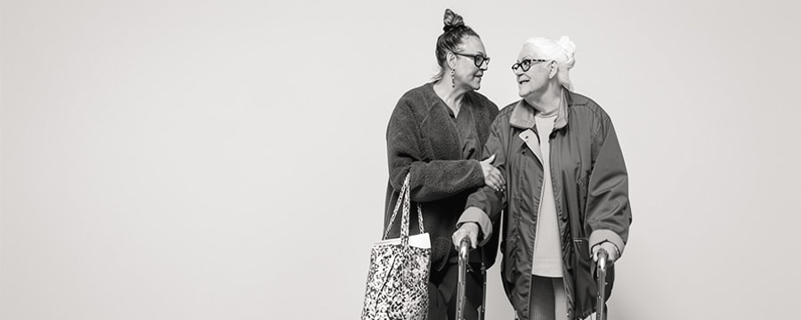 A support worker walking arm in arm with an older woman using a walking frame
