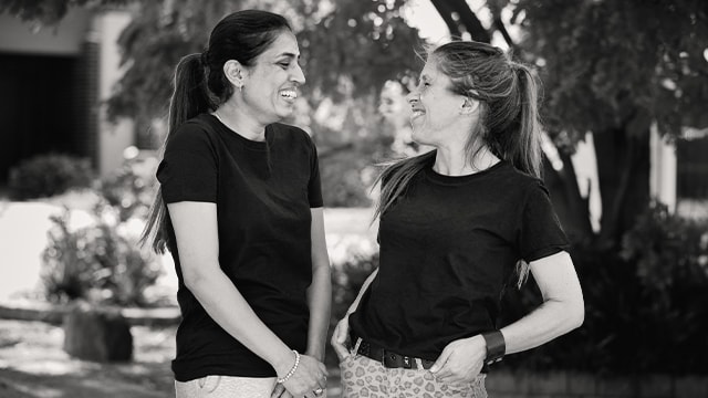 Two healthcare workers in black uniforms laughing together outdoors